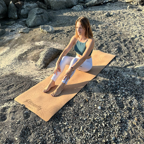 Donna seduta su tappetino yoga in sughero Fitnexfly, ideale per allenamenti outdoor su superfici naturali.