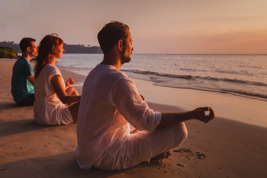 Gruppo di persone che medita al tramonto su una spiaggia, promuovendo il benessere e l'allenamento yoga all'aperto.