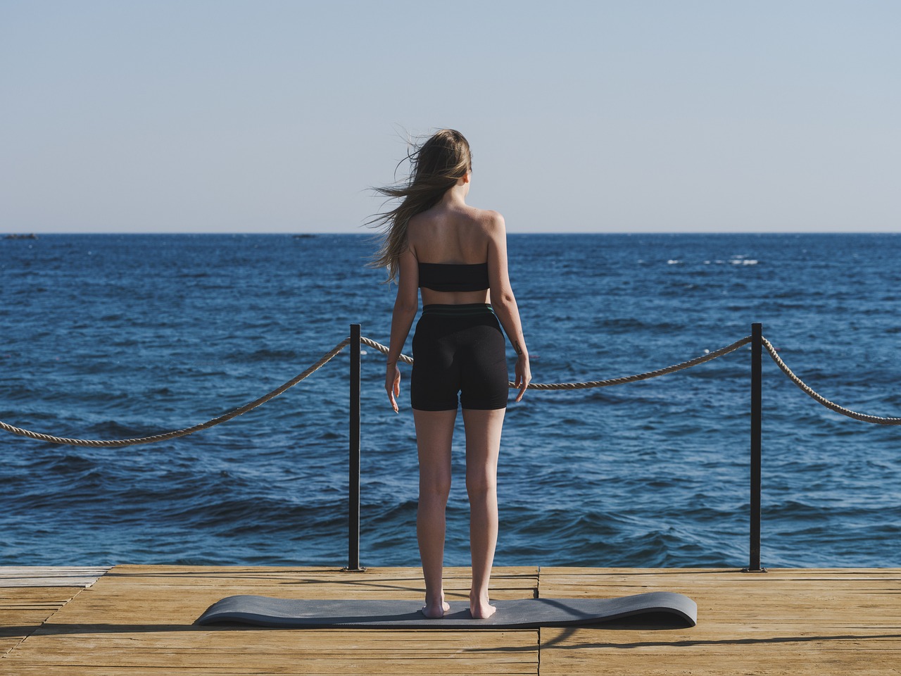 Donna su tappetino yoga pilates che guarda il mare blu