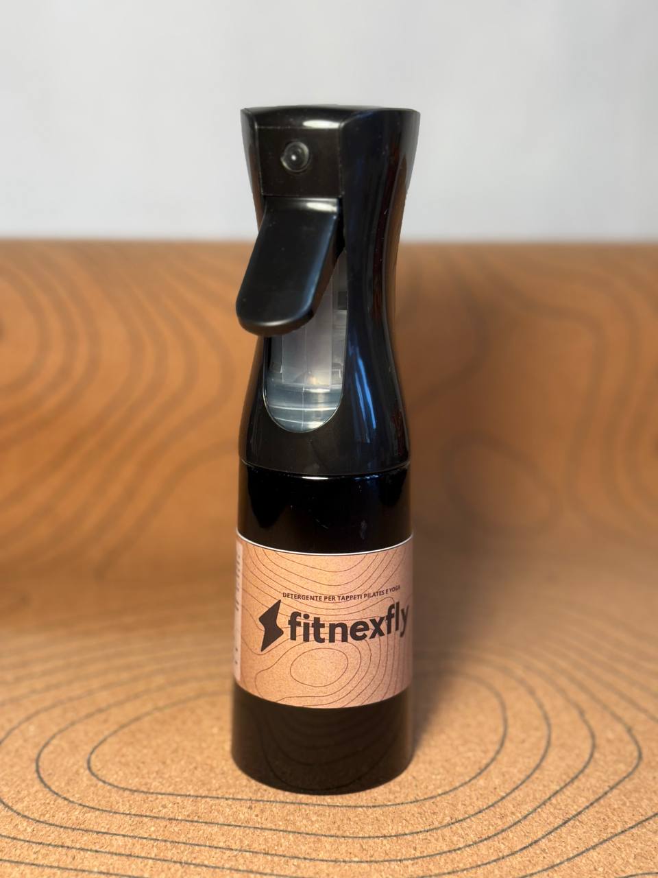 Spray detergente Fitnexfly progettato per la pulizia di tappetini yoga e pilates, mostrato su uno sfondo di sughero, ideale per una manutenzione naturale e accurata.