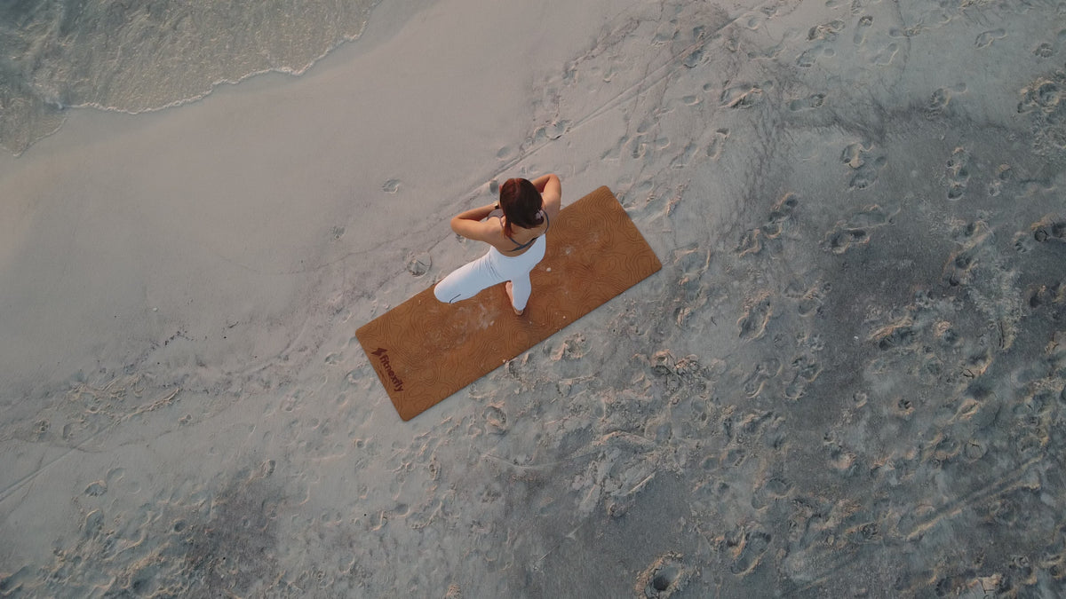 Vista dall'alto ragazza in posizione di equilibrio a una gamba, con gamba piegata a 90 gradi e braccia in preghiera sulla sabbia guardando verso il mare